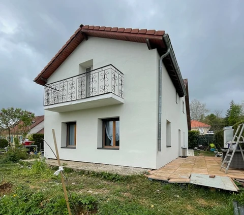 Chantier de construction résidentielle en cours, maison individuelle moderne avec façade blanche, toit en tuiles rouges et balcon à garde-corps métallique décoratif