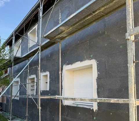 Façade de maison moderne fraîchement rénovée avec murs extérieurs en crépi gris clair sous ciel bleu