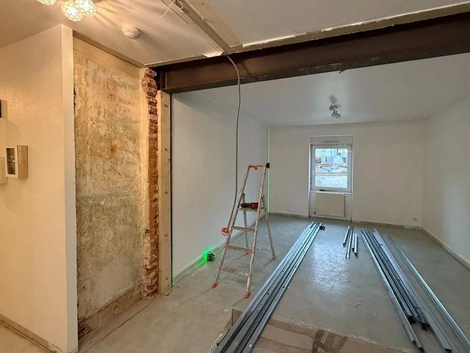 Chantier de construction résidentielle en cours, maison individuelle moderne avec façade blanche, toit en tuiles rouges et balcon à garde-corps métallique décoratif