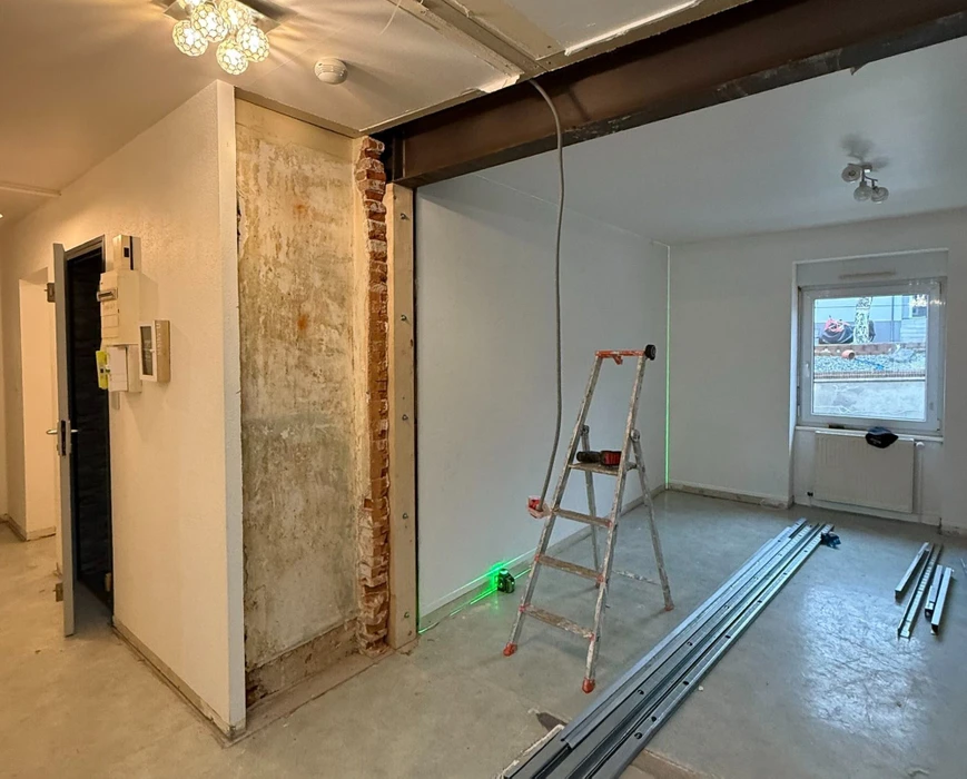 Chantier de construction résidentielle en cours, maison individuelle moderne avec façade blanche, toit en tuiles rouges et balcon à garde-corps métallique décoratif
