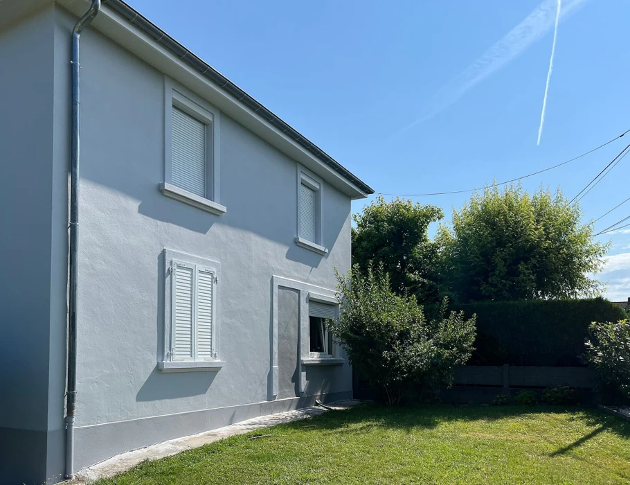 Maison individuelle moderne à deux niveaux avec façade bicolore beige et crème, volets roulants bleus, toiture tuiles grises