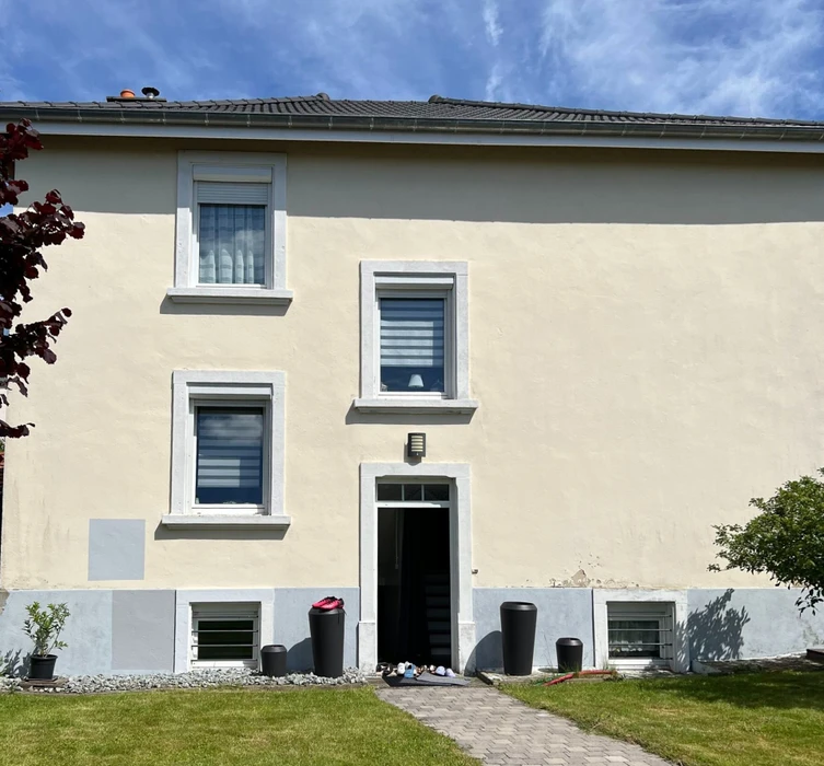 Maison résidentielle moderne avec façade enduit beige et blanc, toiture tuiles grises, gouttières PVC, fenêtre avec linteau décoratif
