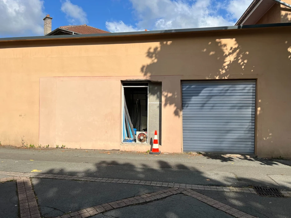 Façade d'immeuble résidentiel moderne avec porte d'entrée vitrée à carreaux et six fenêtres à volets roulants blancs disposées symétriquement sur deux étages