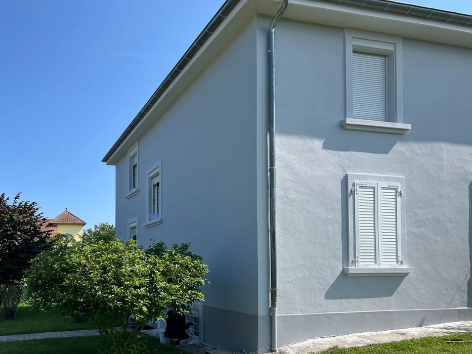 Façade d'immeuble résidentiel moderne avec porte d'entrée vitrée à carreaux et six fenêtres à volets roulants blancs disposées symétriquement sur deux étages