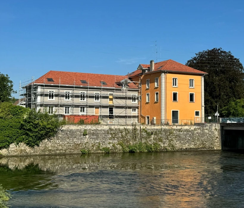 Façade d'immeuble résidentiel moderne avec porte d'entrée vitrée à carreaux et six fenêtres à volets roulants blancs disposées symétriquement sur deux étages