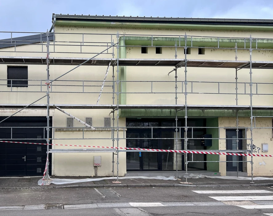 Façade d'immeuble résidentiel moderne avec porte d'entrée vitrée à carreaux et six fenêtres à volets roulants blancs disposées symétriquement sur deux étages