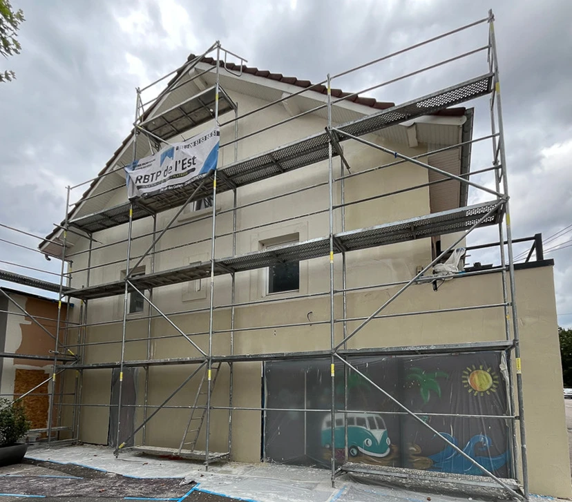 Façade d'une maison résidentielle moderne avec étage, murs enduits beige et gris, fenêtres à encadrements foncés, toiture tuiles terre cuite