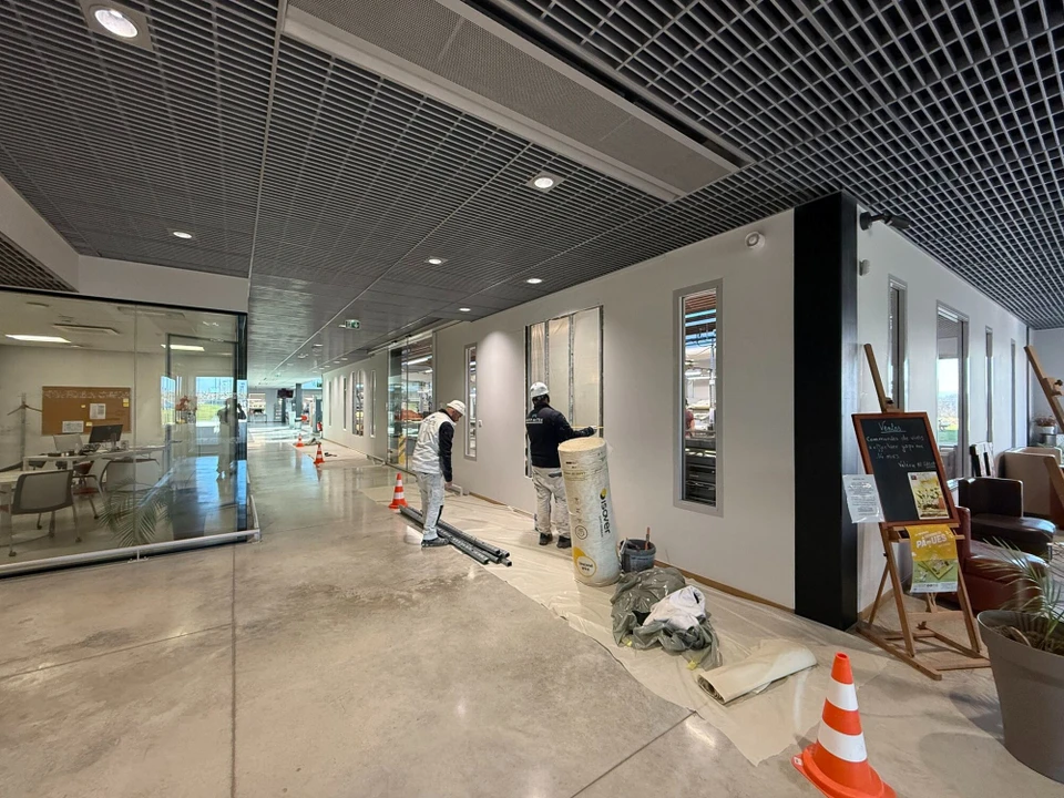 Ouvrier en vêtement blanc utilisant une ponceuse à béton électrique sur sol en béton brut dans un espace intérieur