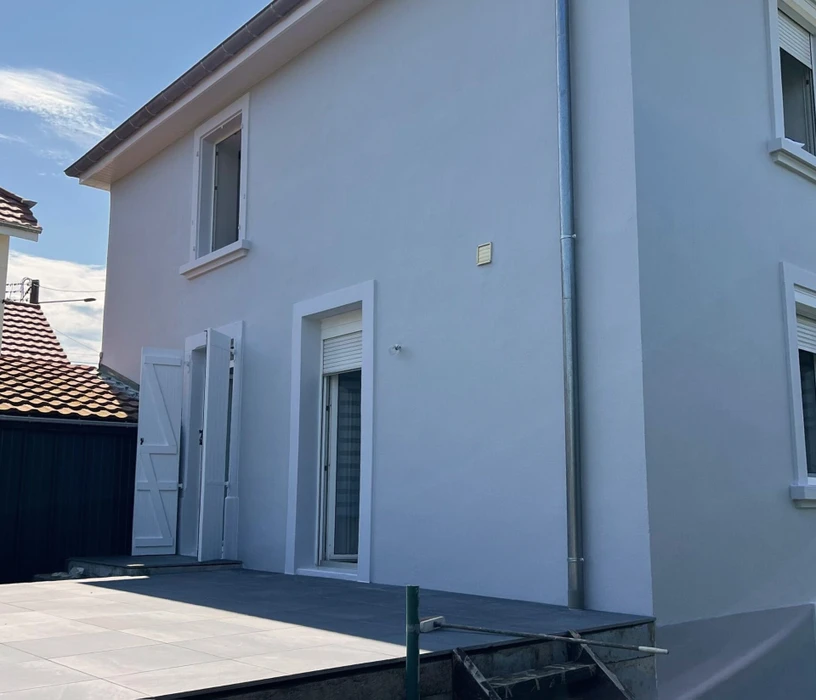 Façade d'une maison résidentielle moderne avec étage, murs enduits beige et gris, fenêtres à encadrements foncés, toiture tuiles terre cuite