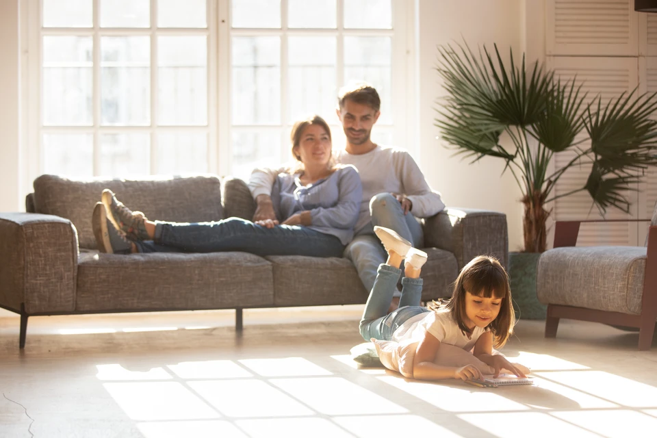 Famille souriante avec enfant dans maison en construction, parents assis au sol tenant clés et téléphone, ambiance chaleureuse et lumineuse